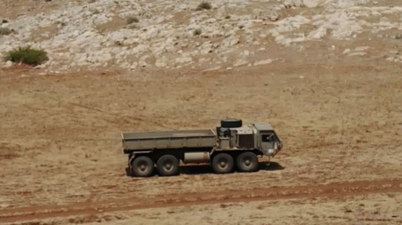 Military truck driving across dry open terrain