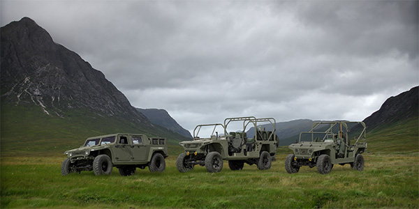 Three light military vehicles in a green mountain valley