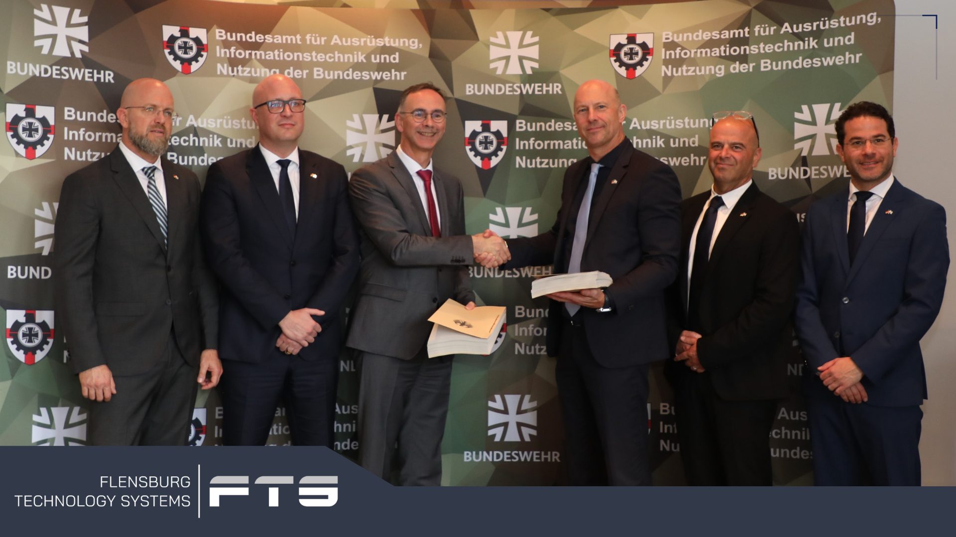 Group of six men at a handshake in front of a Bundeswehr backdrop
