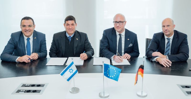 Four men in suits at a signing table with Israeli, EU and German flags