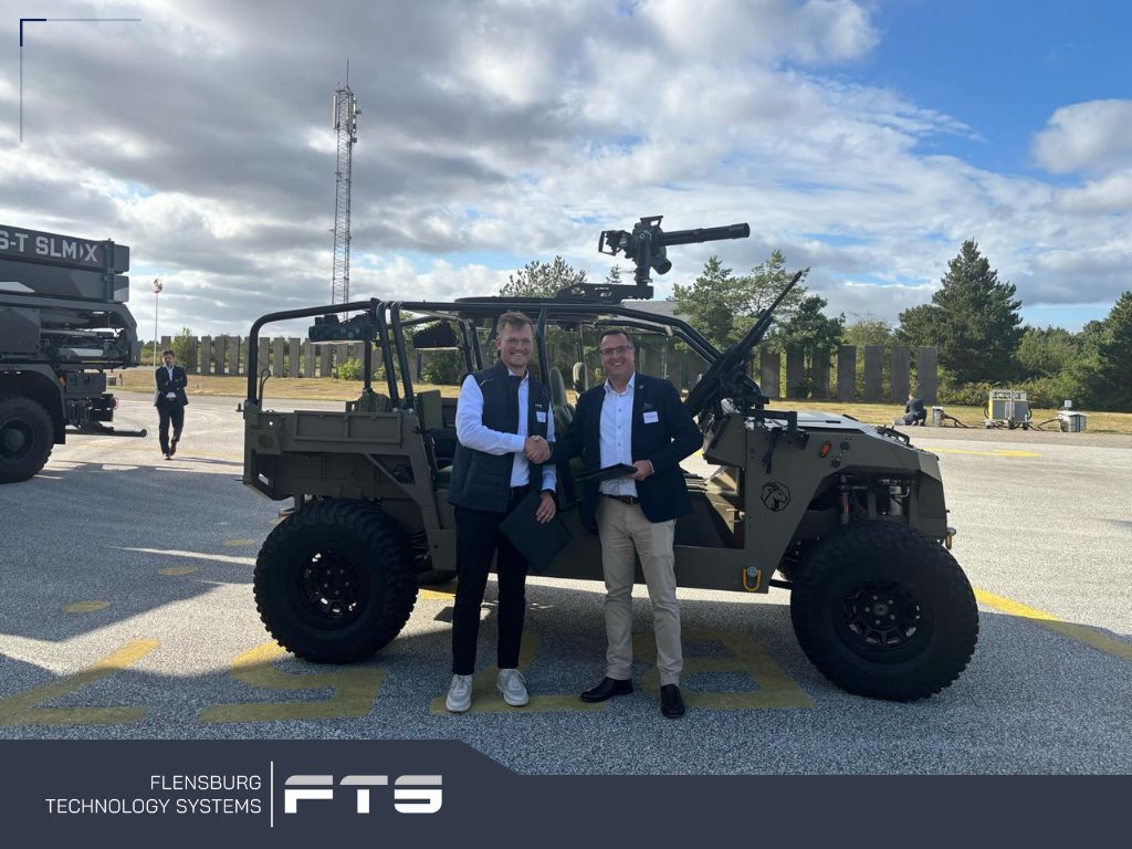 Two men shaking hands in front of a light military vehicle