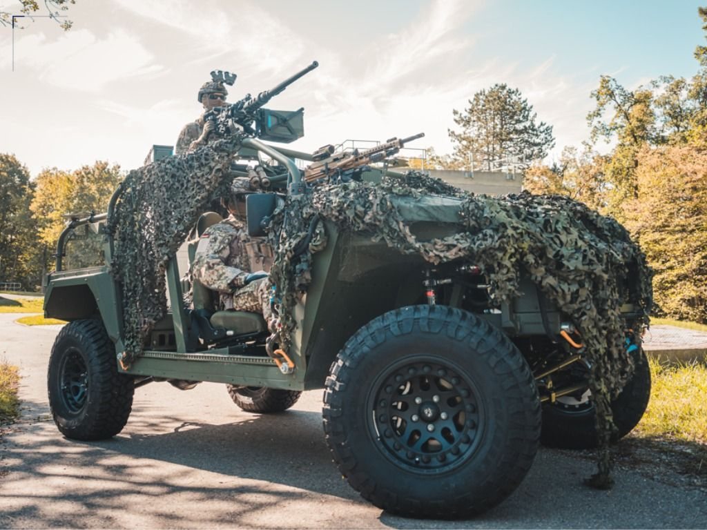 Light military vehicle with camouflage netting and crew on a road