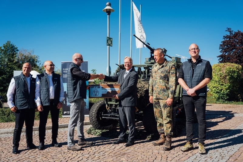 Group of people at a handshake in front of a military vehicle